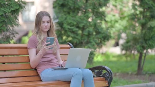 Young Woman Uses Laptop and Phone in Park
