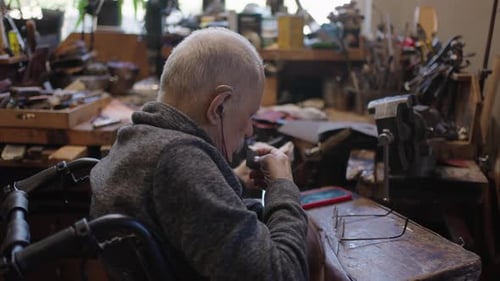 Senior Gray Haired Male Master in a Wheelchair Working at His Workshop Sharpening Japanese Swords