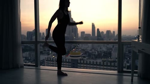 Silhouette of woman stretching at sunset in city apartment