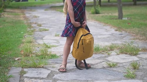 Little Girl in Dress Holds Large Yellow Schoolbag Standing in Green Park Schoolgirl in Uniform