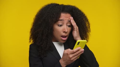 Shocked Woman Reading Bad News on Phone on Yellow Background