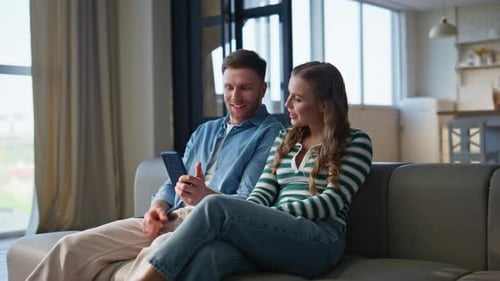 Young Couple Relaxing on Sofa with Smartphone
