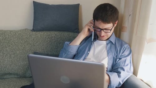 Young Adult Working On Laptop While Talking On Phone