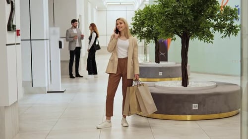 Happy Woman Withshopping Bags Talks on the Phone in a Shopping Center