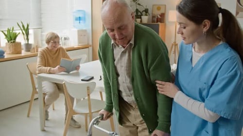 Senior Man Walking with Walker Assisted by Female Nurse in Nursing Home