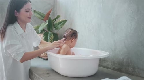 Woman Bathing Adorable Infant in White Tub