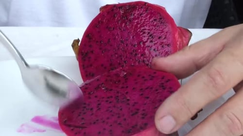 A closeup of a sliced dragon fruit with a man's hands scooping it.