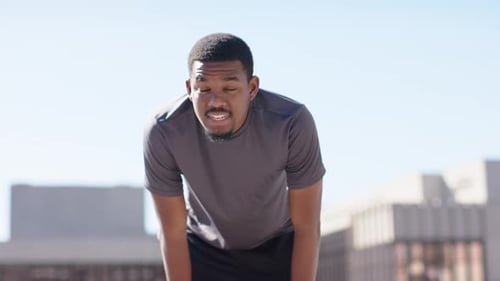 African American man finishing run on roof deck, pausing, steadying breathing and surveying skyline