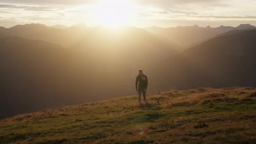 Man Walking Across Field With Mountain Range View At Sunset