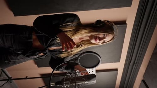 girl singer singing in a recording studio with headphones in front of microphone to create a song
