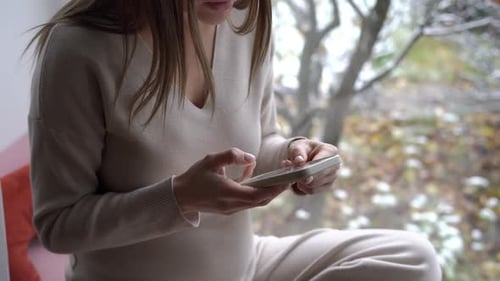 Young Unrecognizable Pregnant Woman Talking Recording Voice Mail Sitting on Windowsill Caucasian