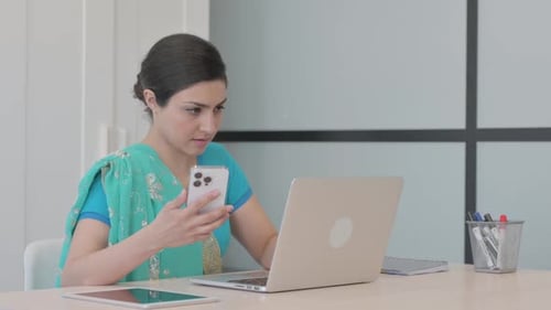 Woman Using Phone and Laptop at Desk
