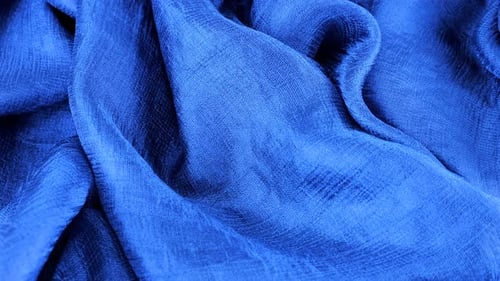 Close-up view of soft folds of dark blue silk muslin rotated on the display case. Textile background