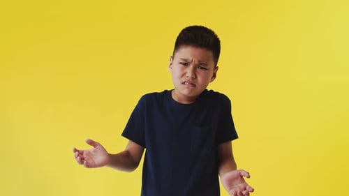 Confused Boy Shrugging on Yellow Background