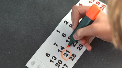 Hand Marking an Important Date on a Calendar Page with an Orange Highlighter