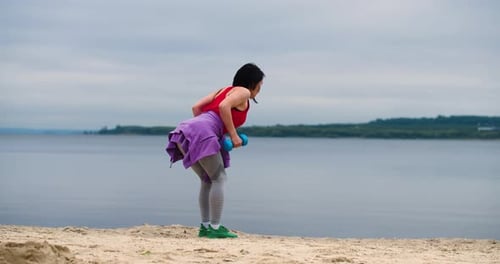Outdoor Back Workout Young Woman Training on the Beach She Trains Her Back Muscles with Dumbbells