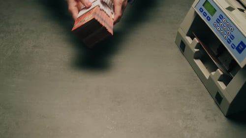 Hands Organize Currency Stacks Near Counting Machine