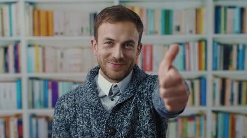 A Man in a Cozy Sweater Gives a Thumbs Up in a Library Setting