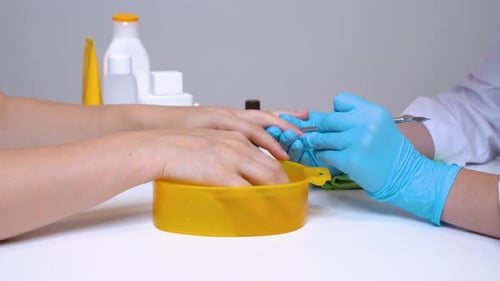 Bei der Nahaufnahme der Hand des Klienten und des Nagelmeisters bei der Bearbeitung der Nägel in Handschuhen wird die Nagelhaut angehoben.