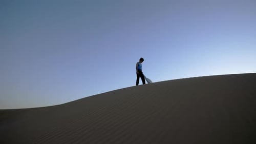 Man walks along sand dune in the desert at sunset