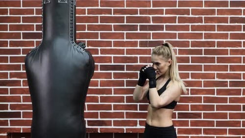 Young Woman Trains in Boxing Ring with Heavy Punching Bag