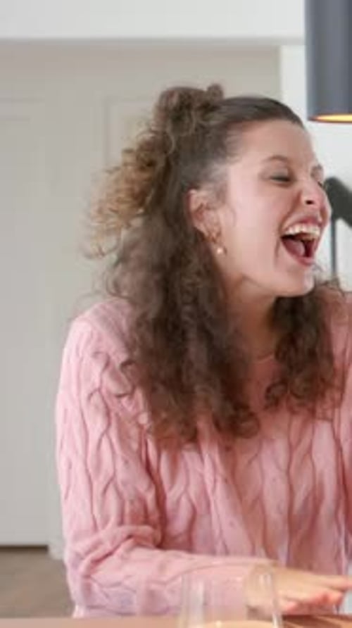 Vertical video: Reacting woman pink sweater celebrating grabbing arm at table with stemless glass