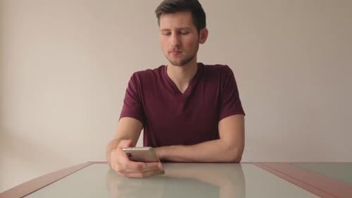 Bored man looking at phone and scrolling, still shot indoor with natural light and minimalist setup