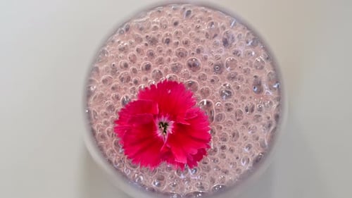 Close up glass with purple cocktail with alcohol and foam, red flower on top
