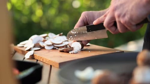 young man cutting mushrooms on wooden board in the garden close up
