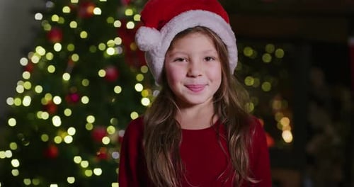 Smiling Girl Wearing Santa Hat by Christmas Tree