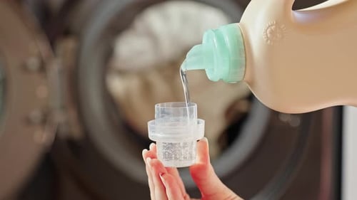 A Woman Pours Liquid Laundry Detergent Into a Cap