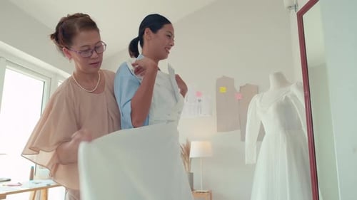 Noiva sorridente experimentando vestido de noiva na frente do espelho junto com a mãe