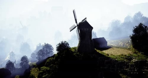 Windmill Sits Atop Hill Surrounded By Misty Landscape in Early Morning Light
