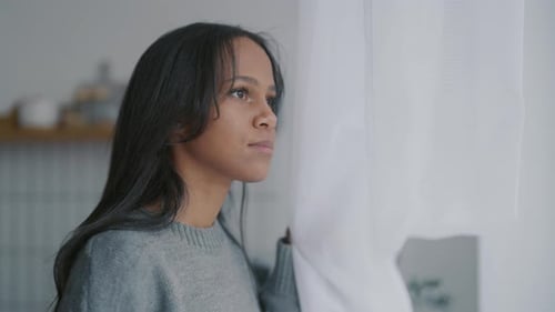 Contemplative Woman Looks Out Window From Home