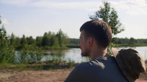Young Man Sitting Near Lake Looking at Water Admiring Scenery View in Sunny Day