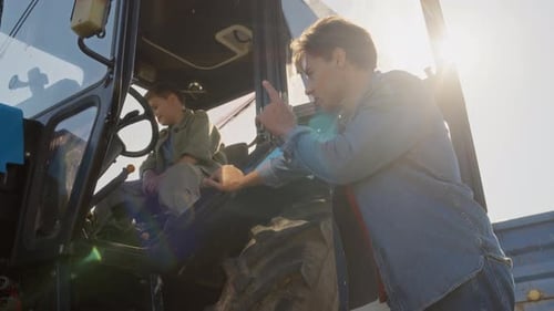 Dad Explaining Machine Operation to Boy Sitting in Tractor Cabin on Farm