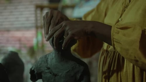 Hands sculpting a clay figure, close-up shot in a cozy studio with warm lighting