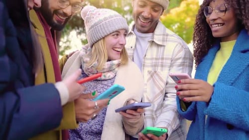 Smiling Friends Looking at Cellphones Together Outdoors