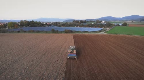 Tractor with harrow system plowing ground on cultivated farm field
