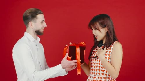 Man Giving Gift to Smiling Woman on Red