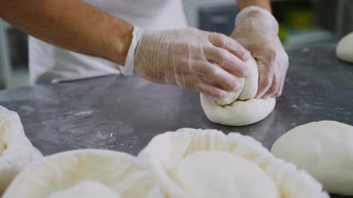Worker shapes dough balls in food preparation