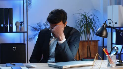 Frustrated Man Working on Laptop in Office at Night