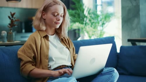 Woman Works on Laptop on Couch in Living Room
