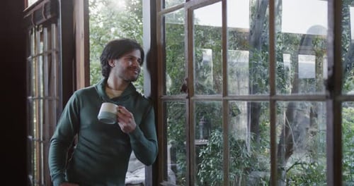 Happy caucasian man with coffee and looking out window at home, copy space, slow motion