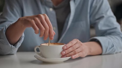 Close Up Of A Cup Cappuccino With Foam, A Girl Sits In A Restaurant Slowly Drinks Coffee, Stirs With