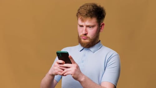 A Teenage Redhead Guy in a Studio Shot Shocked and Staring at His Smartphone