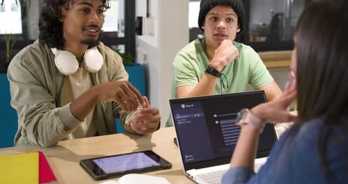 Groupe d'étude diversifié discutant du projet après un message de discussion apparaissant sur un ordinateur portable dans une zone d'étude partagée