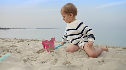 Toddler boy happily playing on the beach and digging sand with a shovel