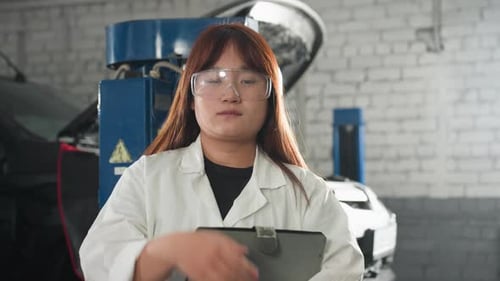 Student Adjusting Protective Glasses While Holding Tablet in Automotive Workshop