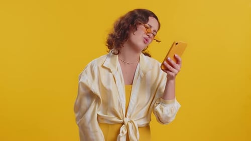 Confused Woman Looking At Cell Phone, Yellow Background
